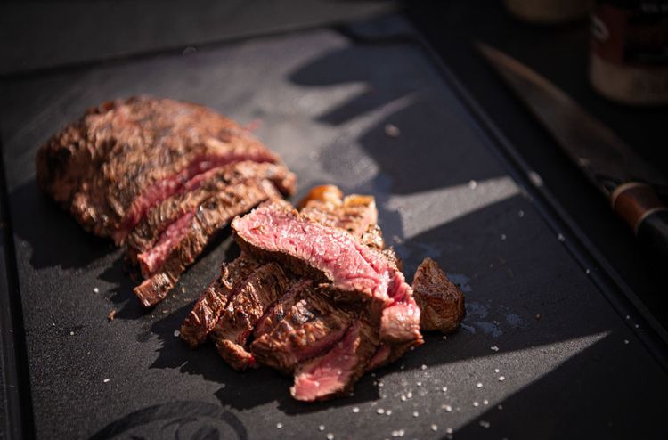 Carne fatiada no ponto sobre a tábua escura, ao lado da faca do chef